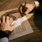 Person holding gold mobile phone in one hand while signing a document with the other