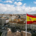 The Spanish national flag flying from a tall building over a cityscape.